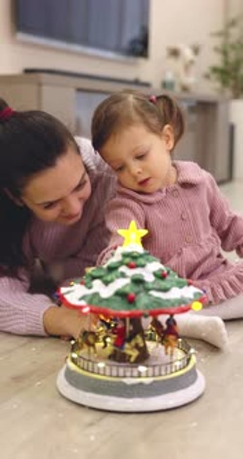 Mother and Little Child Girl Looking at Christmas Musical Carousel Toy