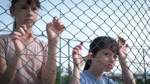 Two Young Girls Behind a Chain Link Fence