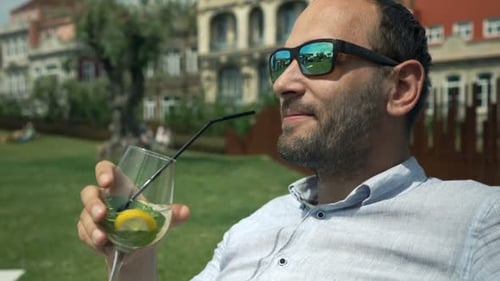 Young Man Relaxing and Drinking Cocktail in Garden in Cafe 30s