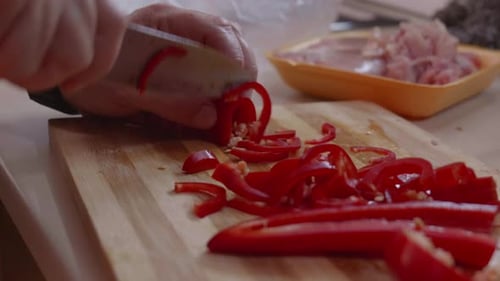 Knife slices red bell pepper on wood board