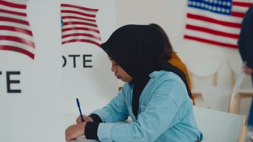 Muslim Woman in Hijab Writing on Ballot in Booth at American Polling Station
