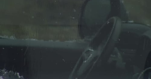 Snow in front of a car window, steering wheel and mirror in shot, static