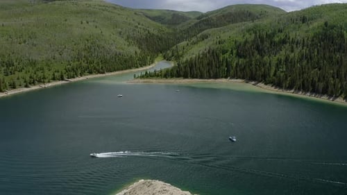 Revealing drone shot of boats floating on a mountain reservoir on a sunny summer day, down panning s