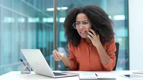Angry african american businesswoman arguing talking on mobile phone at workplace in office.