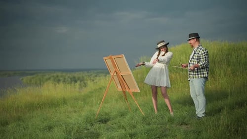 Painter and Woman in White Dress Discussing Canvas in Grassy Field