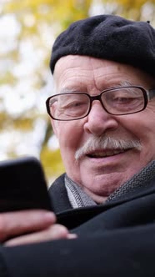 An Elderly Grandfather Enjoys Using His Smartphone Surrounded By a Stunning Bright Autumn Park