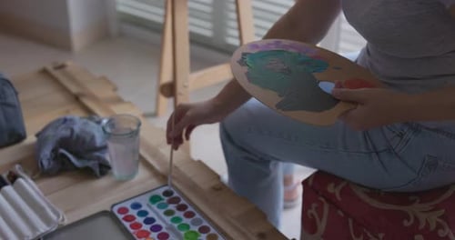 Female artist painting on canvas during sunny day at home - Woman mixing watercolors