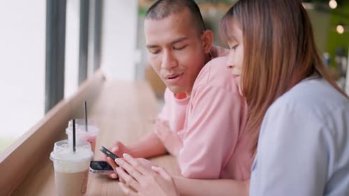 A man drinks a drink at a restaurant and looks at his lover using a smartphone to surf the internet.