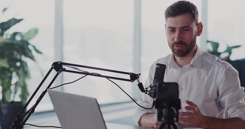 Man Recording Podcast with Laptop, Microphone, and Smartphone