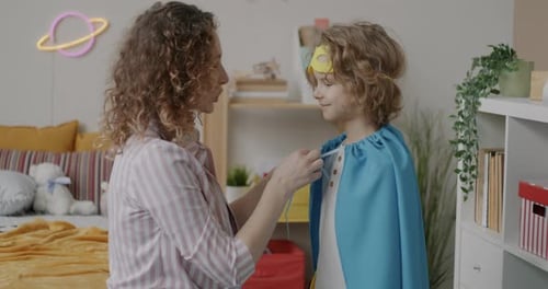 Woman Helps Child With Superhero Costume at Home