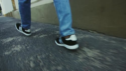 Männerbeine in Jeans und Turnschuhen laufen schnell auf dem Bürgersteig der Stadt