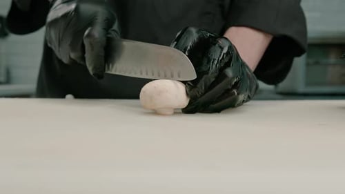Close-up of a sushi maker in gloves cutting a mushroom on a white board in a professional kitchen