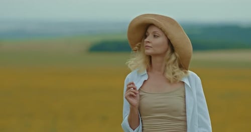 Portrait d'une belle femme coiffée d'un chapeau se promenant dans le village tenant un brin d'herbe dans ses mains