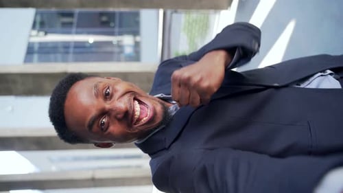 excited black businessman rejoices in victory looking at camera while standing outside office