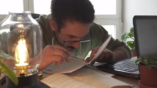 Close up of male studying and taking notes with laptop and papers
