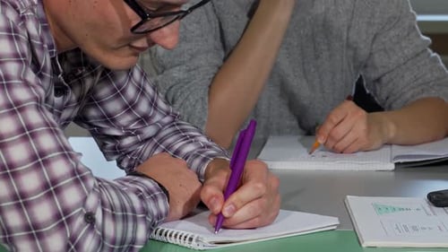 Konzentrierter junger Mann, der während des Studiums fleißig in sein Lehrbuch schreibt