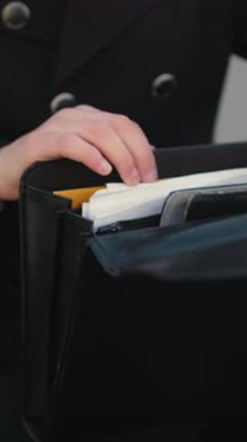 Close Up of Hand in Black Clothing Opening Briefcase and Searching Documents Outdoors