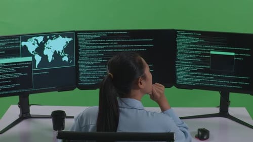 Back View Of Asian Woman Thinking While Write Code With Multiple Computer Screens In Green Screen