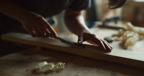 Female woodworker carves wooden piece in bright workshop sunlight