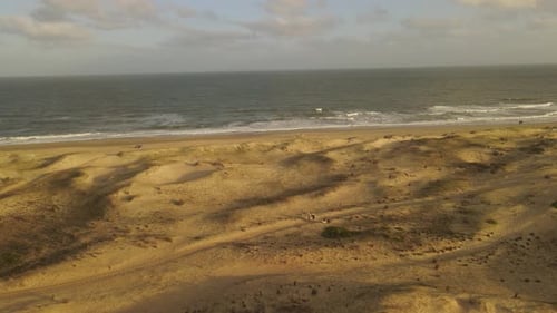 People walk through sand dunes on beach, rotating aerial view