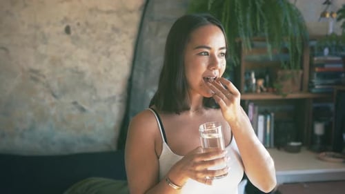 Woman Taking Pill with Water in Sunny Home