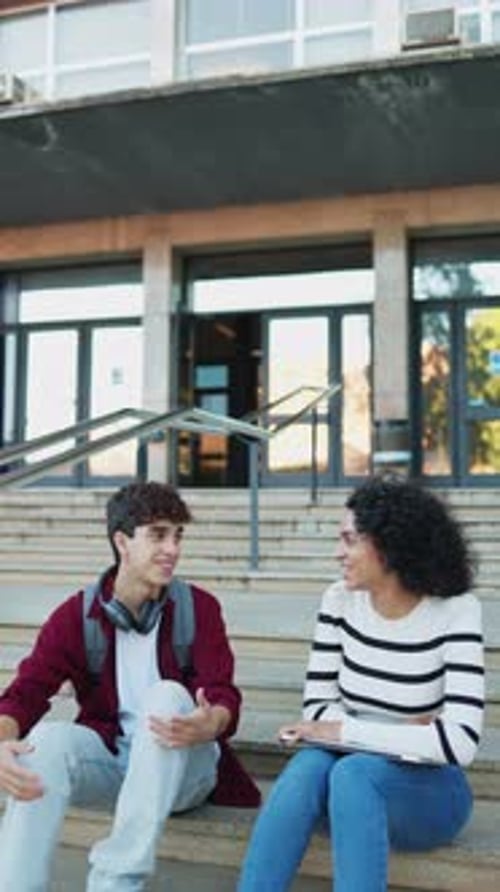 Cheerful multiethnic student friends talking while sitting on the stairs of the university