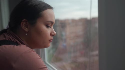 Woman Looks Out Apartment Window Thoughtfully