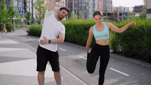 A Young Positive Sportive Couple Does Morning Exercises Before Workout in the City Park Area Among