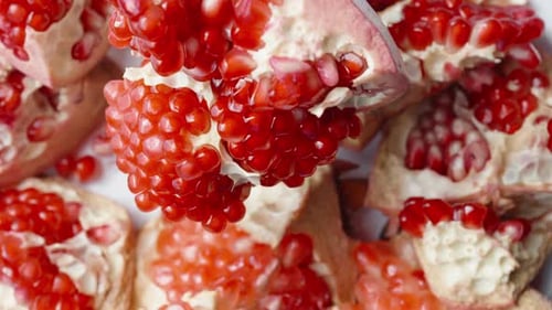The pomegranate fruit, divided into parts, rotates against the background of pieces with red grains,
