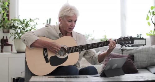 Mujer adulta madura aprendiendo a tocar la guitarra en casa con un vídeo tutorial