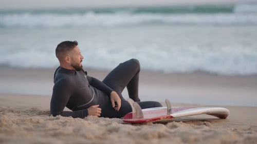 Surfer entspannt am Sandstrand mit Surfbrett und Blick auf die Meereswellen