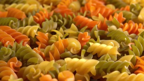 Multicolored italian pasta Fusilli or Rotini rotating in close up background sun light side view