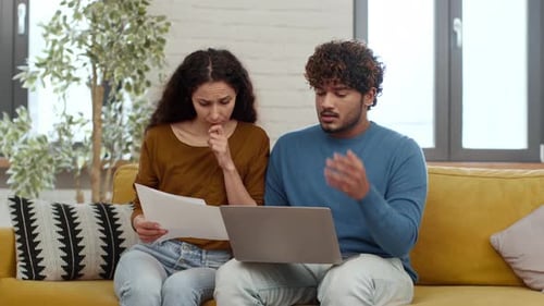 Couple Discussing Important Documents at Home While Sitting on a Yellow Sofa