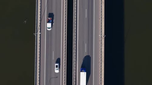 Top-down aerial view of a highway bridge with moving cars and a freight truck crossing over a river
