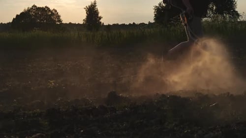 Farmer Walking on Cultivated Field Spraying Pesticides with Manual Knapsack Sprayer at Sunset