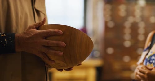 Craftsman passes wooden bowl to woman in shop