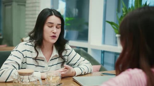 Mujer explicando algo a su amiga en una mesa de un café