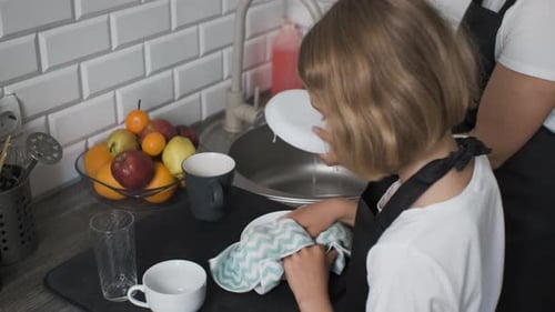 Child Helping Wash Dishes with Adult in Kitchen