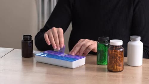 Woman Fills Pill Organizer with Medications at Table