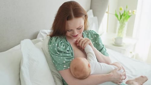 Loving Woman Breastfeeding Infant in Bed at Home