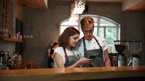 Two employees stands in the cafe. Guy putting cups with cofee on the table
