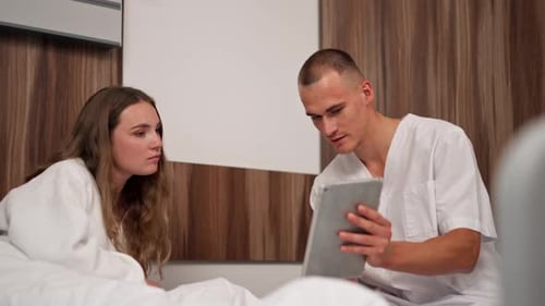 in Modern Clinic in a Bright VIP Room a Young Girl in a White Coat Lies on the Bed Consulting a