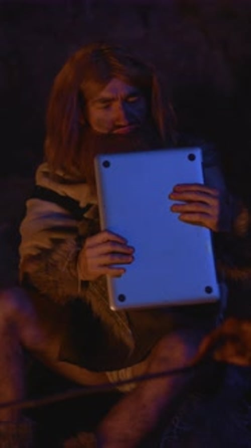 A Humorous Postcardstyle Image of a Caveman Using a Modern Laptop in a Funny Setting