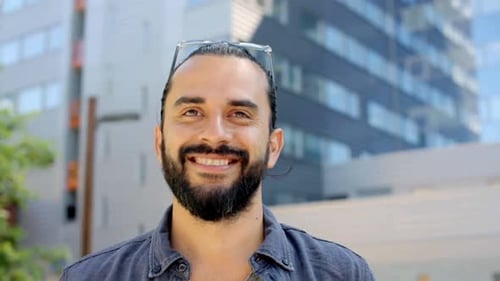 Happy young man with beard smiling on sunny city street in europe