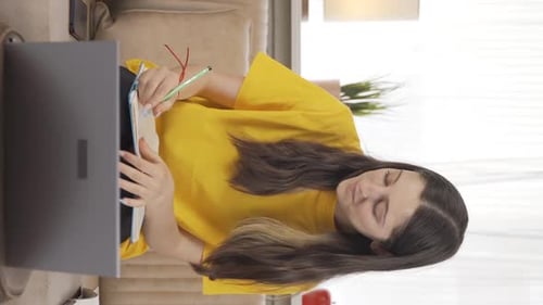 Woman Taking Notes While Using Laptop Indoors