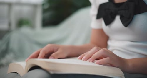 Junge asiatische Frau sitzt entspannt auf der Couch und liest ein Buch im Wohnzimmer.