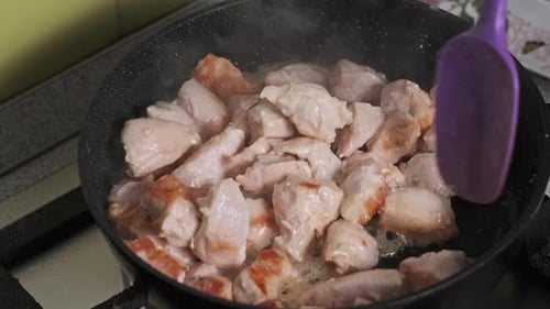 Pieces of Chicken Meat are Fried in a Frying Pan in Home Kitchen