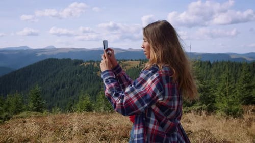 Young woman captures breathtaking mountain vista with smartphone on summer holiday