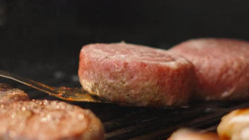 Close Up Flipping Large Raw Beef Burger on Simmering BBQ Grill with Other Patties Cooking.