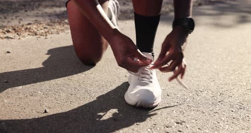 Man Tying Shoe Laces on Paved Road